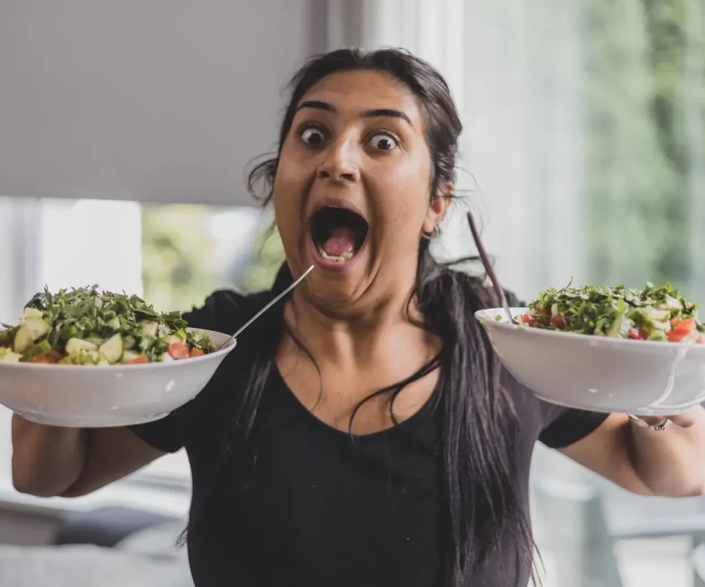 Mulher com saladas e expressão engraçada porque como saudável e não emagreço?