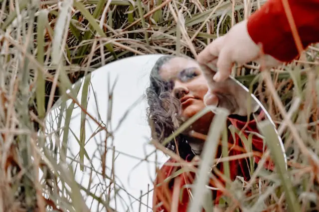 Mulher a olhar-se ao espelho no meio da natureza, imagem sobre autoimagem e sabotadores do emagrecimento