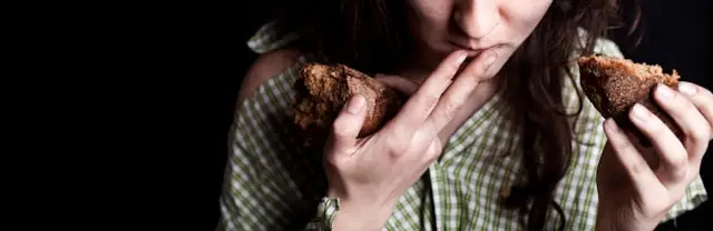 Mulher a comer pão com as mãos, imagem sobre fome emocional e sensação de fome mesmo depois de comer